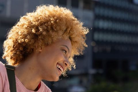 Joyful african american teen laughing outdoors with curly blonde afro and urban bokeh