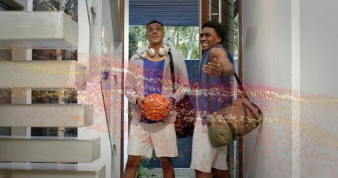 Two young athletes entering doorway holding basketball and duffel bag smiling friends
