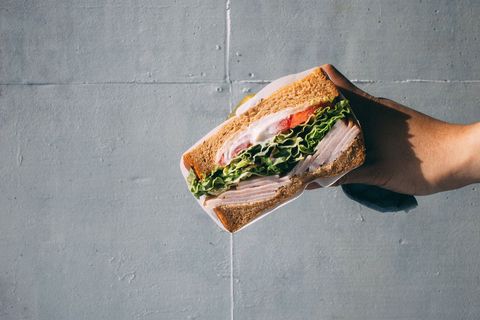 Hand holding fresh turkey sandwich with lettuce and tomato against concrete background