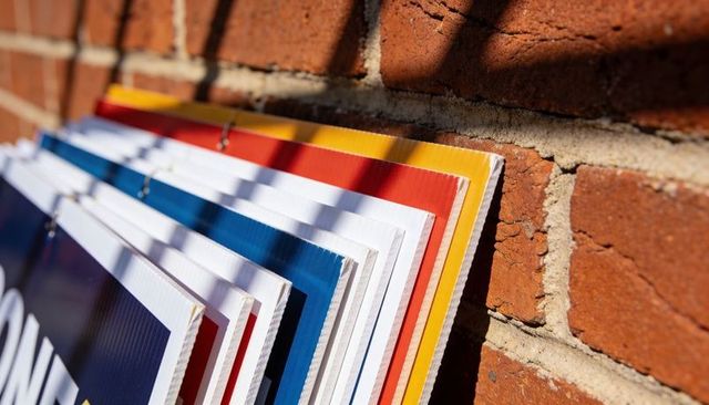 Colorful corrugated sign panels leaning against red brick wall, casting diagonal shadows