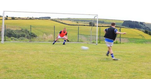 Youth Soccer Practice on Rural Pitch with Goalkeeper and Player Kicking