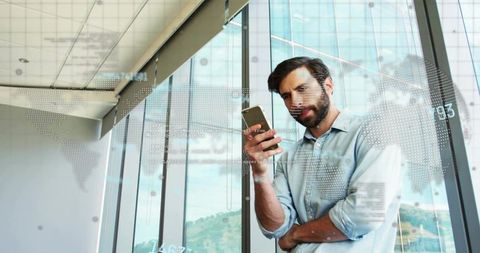 Businessman reviewing mobile analytics with digital world map overlay in modern office