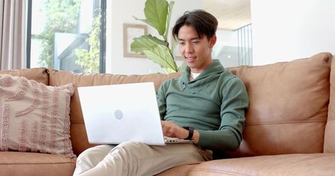Asian Male Relaxing with Laptop on Cozy Couch at Home