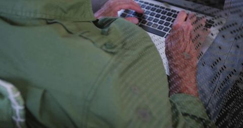Senior man typing on laptop wearing green jacket and jeans close-up hands and keyboard