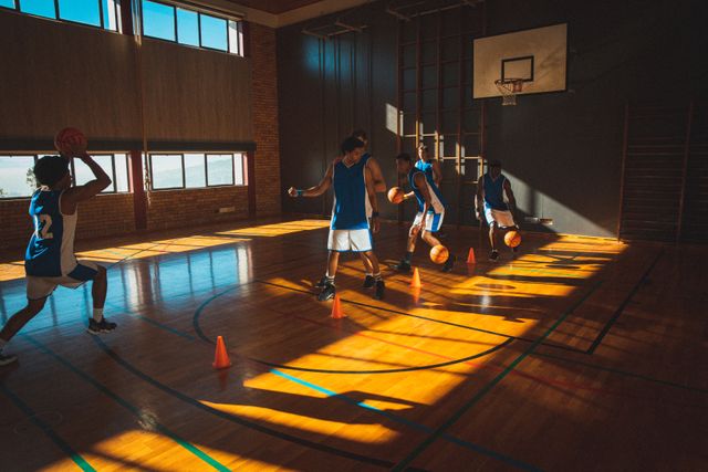 Diverse male basketball team practicing dribbling balls between cones in sunny gym - Download Free Stock Photos Pikwizard.com