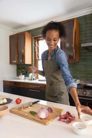 African american woman chopping red onion and smiling while cooking on kitchen island