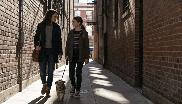 Mother and daughter walking terrier in sunlit urban alley, chatting and smiling