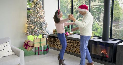 Couple dancing beside decorated Christmas tree and wood stove in cozy modern living room