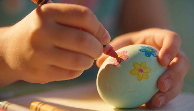 Child decorating pastel easter egg with crayon flower designs closeup in warm light