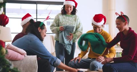 Diverse friends exchanging warm sweater gifts by festive tree