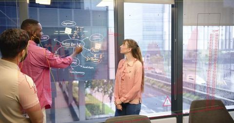 Team brainstorming on glass board with presenter writing business plan in modern office