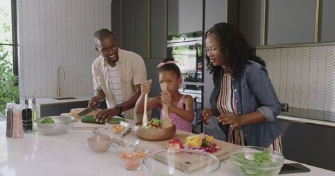 African American family preparing healthy meal at kitchen island, child mixing salad