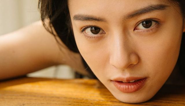 Closeup portrait of asian woman resting face on wooden table with soft natural light, intimate