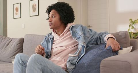 Mid-adult african american man sitting on sofa wearing denim jacket and pink hoodie