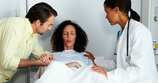A Caucasian man and a biracial woman in labor are being assisted by an African American female doctor, with copy space. The image captures a moment of childbirth support in a medical setting, emphasizing the roles of healthcare professionals and family during delivery.