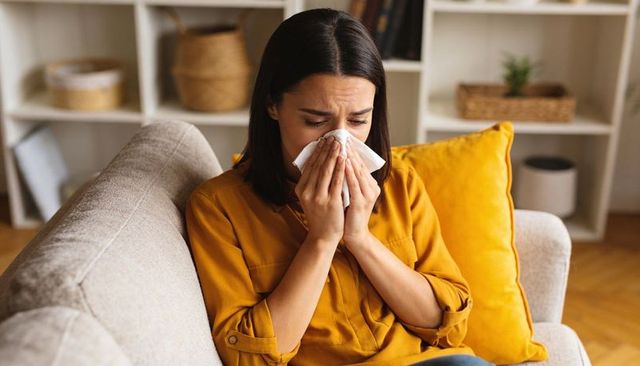 Young woman blowing nose and crying on couch wearing mustard blouse with yellow pillow