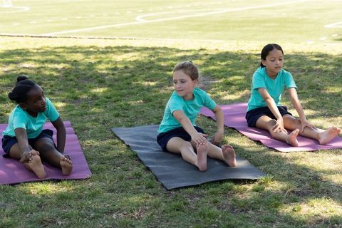 Young girls stretching on yoga mats outdoors on grassy school field during pe class