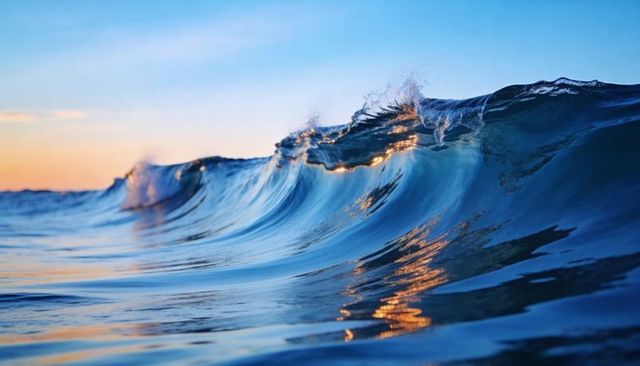 Cresting blue ocean wave catching golden sunset light, glassy sea-level surf