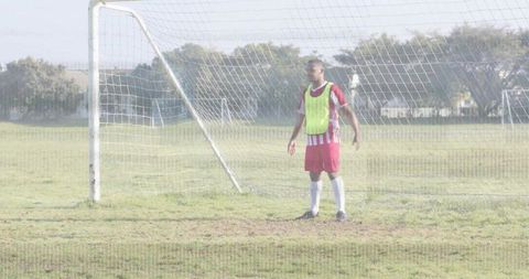 Goalkeeper standing in goal during soccer training on grass field wearing fluorescent bib