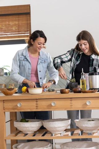 Friends cooking together at wooden kitchen island preparing fresh herbs with mortar