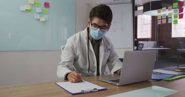 Doctor Taking Notes while Working on Laptop in Office - Download Free Stock Images Pikwizard.com