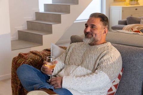 Senior man relaxing on sofa holding wine glass in cozy modern living room interior