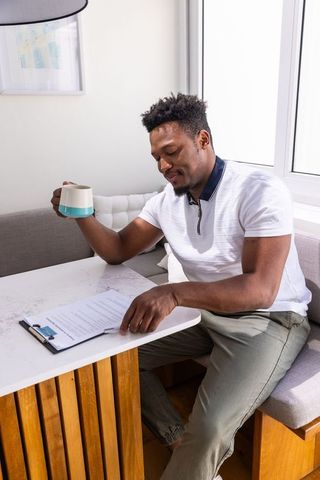 African american man reviewing documents while holding mug at sunlit kitchen nook