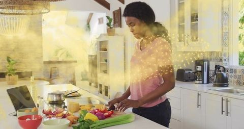 Chopping colorful bell peppers on kitchen island with tablet and golden light accents