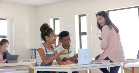 Engaged High School Students Collaborating with Teacher on Laptop