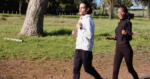 Jogging duo recording outdoor workout with smartphone gimbal on sunny park trail