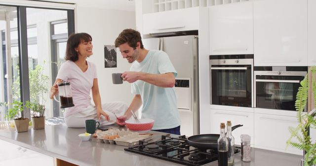Young couple enjoying morning coffee while preparing breakfast together in a modern kitchen. Ideal for lifestyle, home, and relationship-themed concepts. Great for promoting kitchen appliances, home decor, and healthy living blogs.
