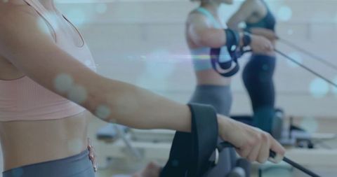 Closeup pulling reformer straps in pilates class, women wearing sports bras and leggings