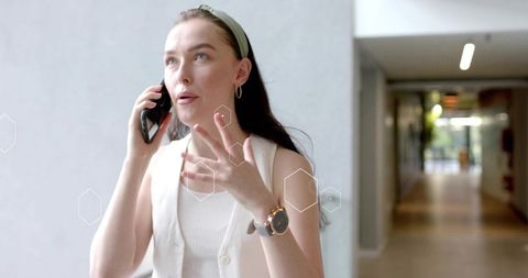 Professional woman talking on smartphone in office corridor with hexagon overlay