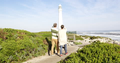 Senior Couple Enjoying Leisurely Walk by Beautiful Seaside Lighthouse