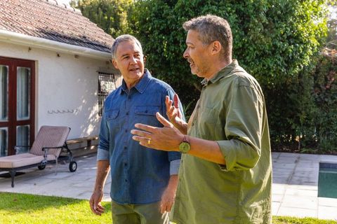 Mature male friends enjoying casual conversation by backyard pool