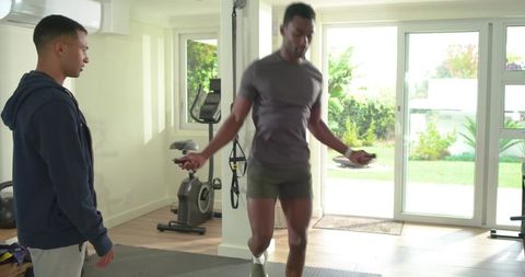At-home personal training: male client jumping rope while coach supervising gym session