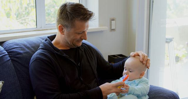 Father Feeding Baby with Spoon on Couch by Window - Download Free Stock Images Pikwizard.com