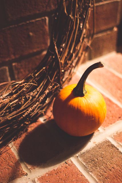 Perfect for autumn-themed designs and social media posts, this image showcases a vibrant orange pumpkin against a rustic brick wall with decorative twigs, evoking a cozy fall atmosphere. Ideal for marketing fall festivals, decor products, or Halloween events.