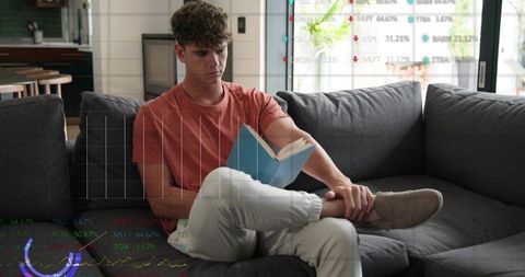 Young man reading book on sofa with digital data overlays, remote work and study concept