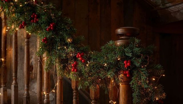Festive pine garland draping rustic wooden banister with warm fairy lights and red berries
