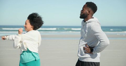 Couple stretching on sunny beach wearing smartwatches and activewear for seaside workout
