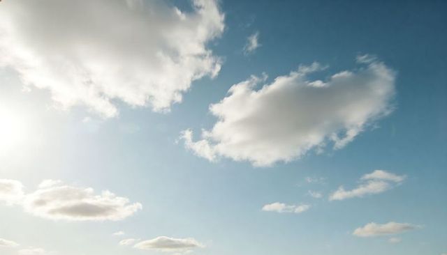 Sunlit cumulus clouds drifting over clear blue sky with soft lens flare and airy horizon