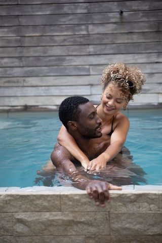 Couple hugging in backyard pool with wood wall, relaxing sunlit summer romance and lifestyle
