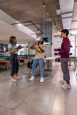 Diverse startup team testing vr headset in open office lounge, colleagues guiding demo