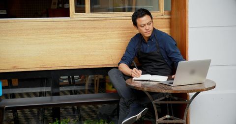 Young Asian Man Working on Laptop at Outdoor Cafe