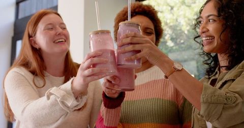 Diverse friends toasting mason jars in modern kitchen