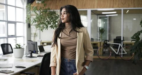 Indian businesswoman standing in modern office wearing beige blazer and smartwatch