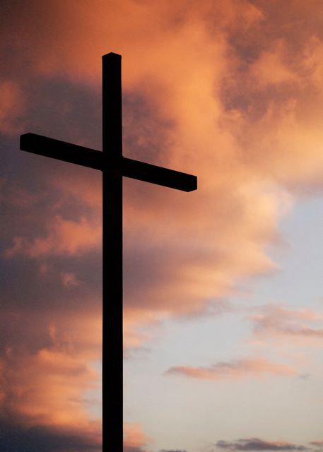 Cross silhouetted against vibrant, dramatic sunset sky with colorful clouds. Ideal for themes of faith, spirituality, and hope. Can be used in religious publications, inspirational posters, and social media content.