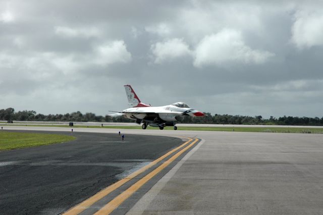 U.S. Air Force Thunderbird F-16 fighter jet performing a landing at Kennedy Space Center. Sky cloudy with flexible asphalt and helicopter landing pad. Part an air show for World Space Expo part NASA’s 50th Anniversary officially showing both past present visions in aviation and space exploration. Could used websites covering aviation, military history UAV exhibitions also promotional material informative classes or extensive galleries aerospace achievements.