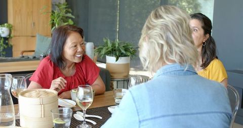 Senior chinese woman laughing and gesturing while sharing meal with friends around table